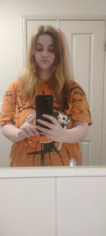 Woman wearing orange tie dye shirt and lightened hair taking a bathroom mirror selfie