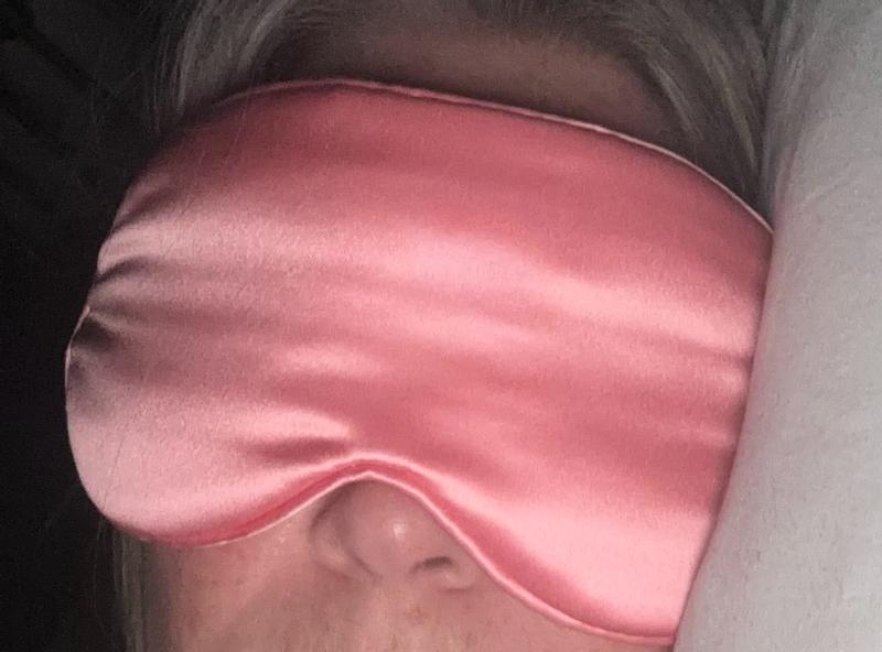 Soft rose-pink silk blindfold gently covering closed eyes, serene expression of deepening relaxation and trust